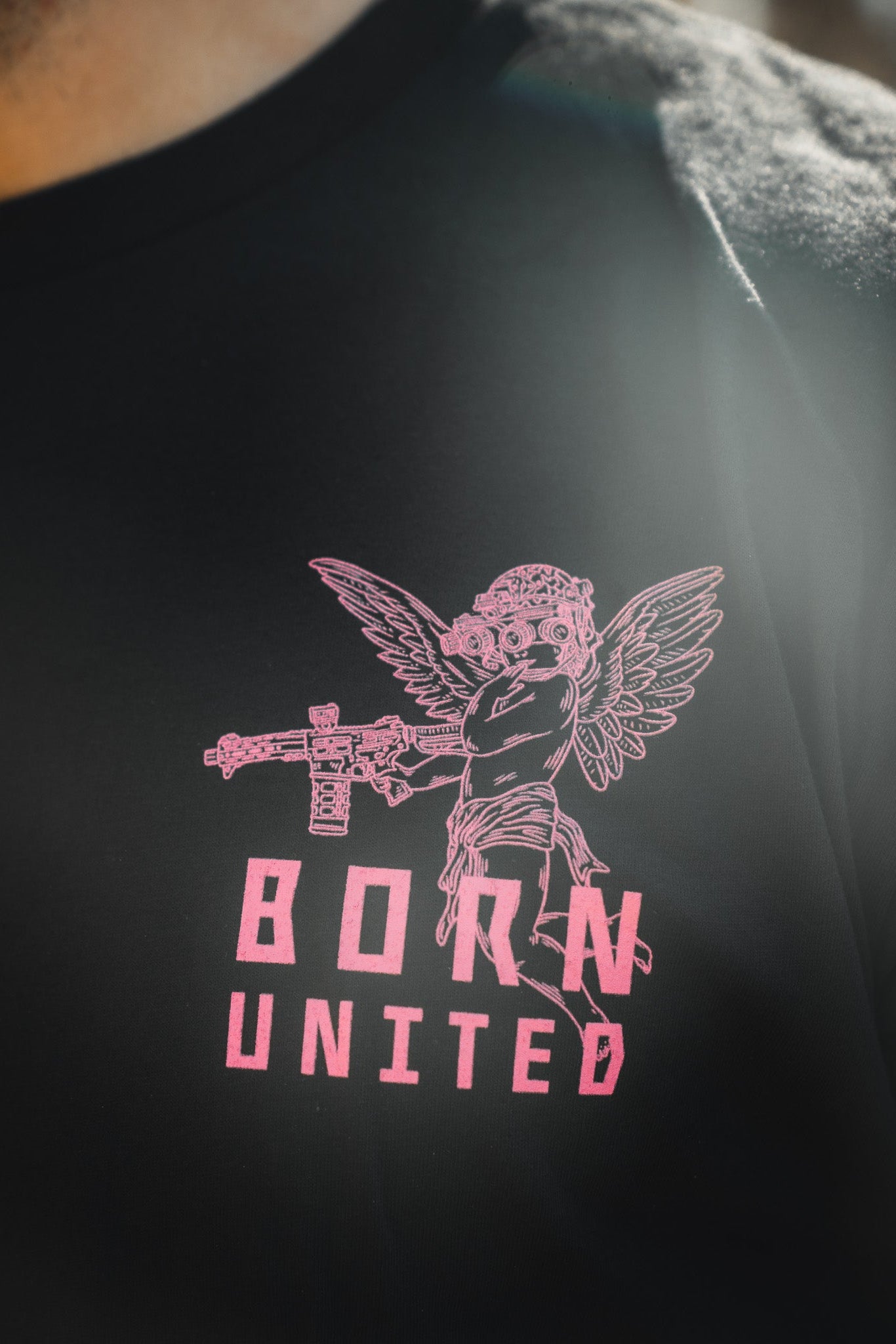 The black "Cupid’s Shot" tee by Born United Private Label features a pink tactical cupid—winged, goggled, with a rifle—and "BORN UNITED" printed below.