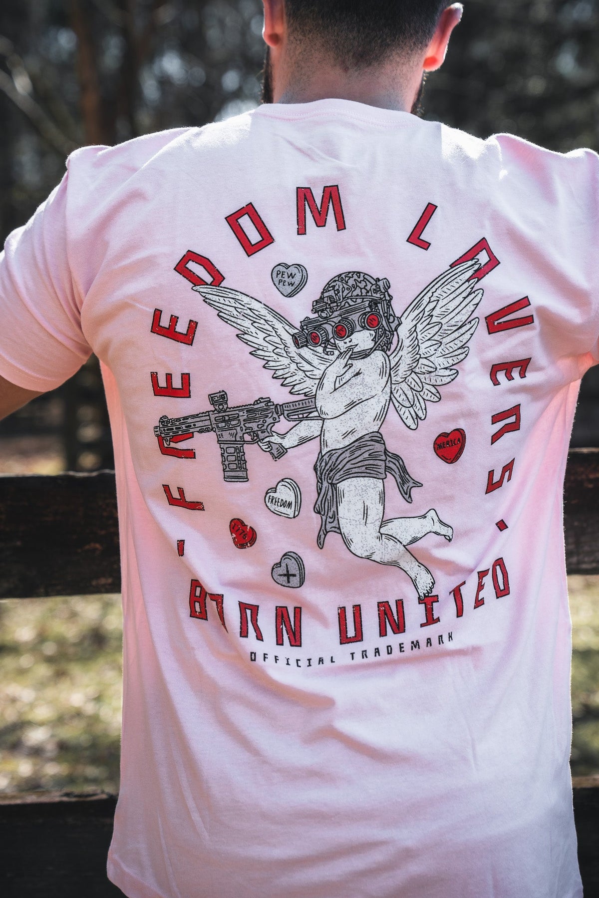 Wearing the Cupid’s Shot V2 by Born United Private Label—a white tee with a tactical cupid cherub, bold red "FREEDOM LOVERS" and "BTRN UNITED" text, plus unique symbols—makes a striking Valentine’s Day statement.