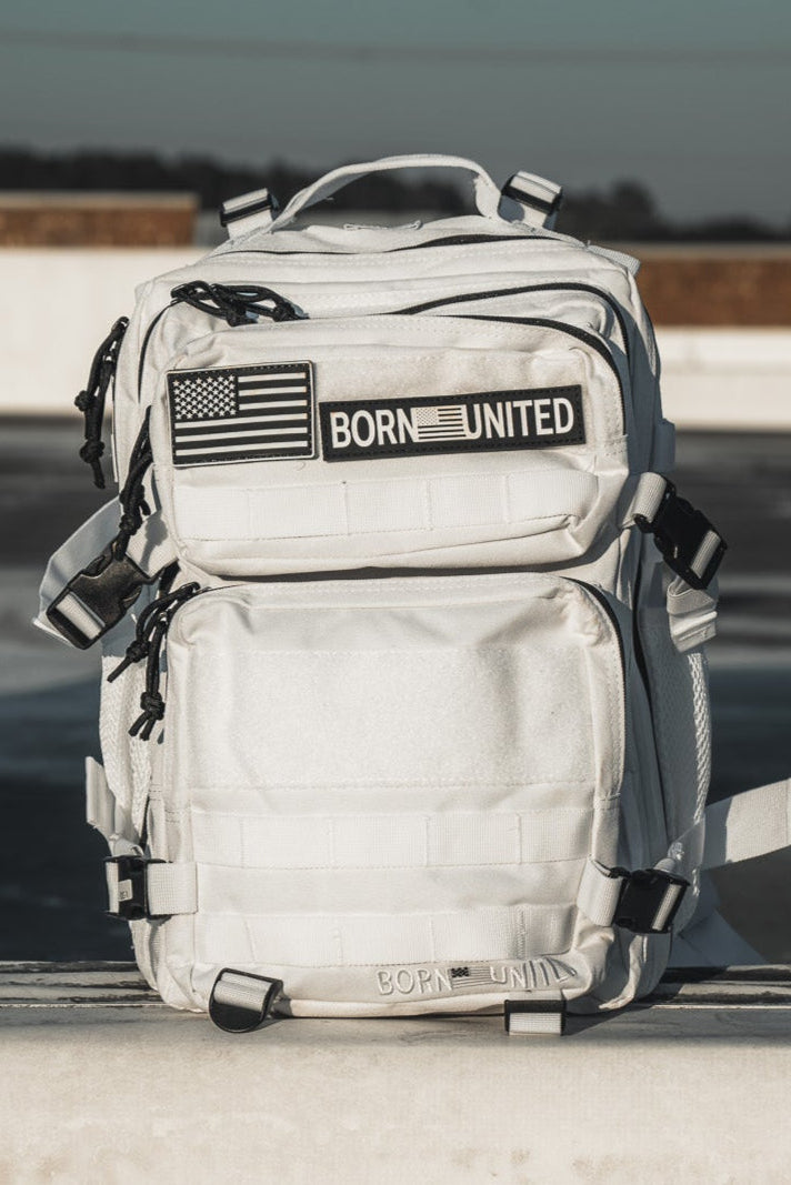 The Storm Trooper Tac-Pac - 25L by Born United Private Label sits upright on concrete, showcasing multiple compartments, black zippers, a U.S. flag patch, and "BORN UNITED" text—evoking classic Star Wars Storm Trooper style.