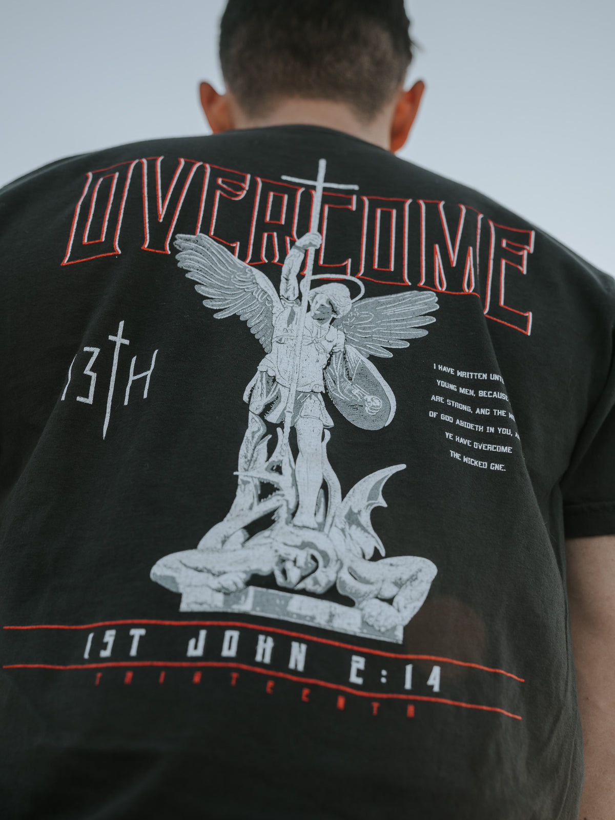 Young men will like the Overcome Premium Tee by 13th, a black T-shirt with red OVERCOME and 13TH, featuring an angel with a sword over a fallen figure. The message from 1st John 2:14 is powerful and grounded in scripture.