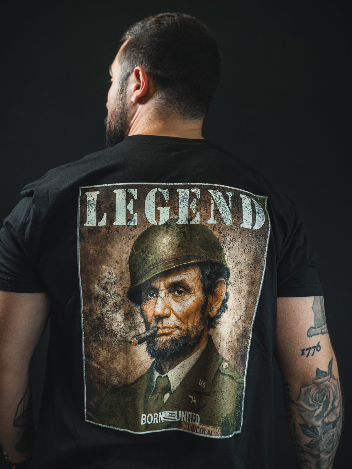 A man with tattoos faces away, wearing the Legend - Lincoln tee by Born United Private Label, featuring Abraham Lincoln in military gear with LEGEND above—ideal for history fans.