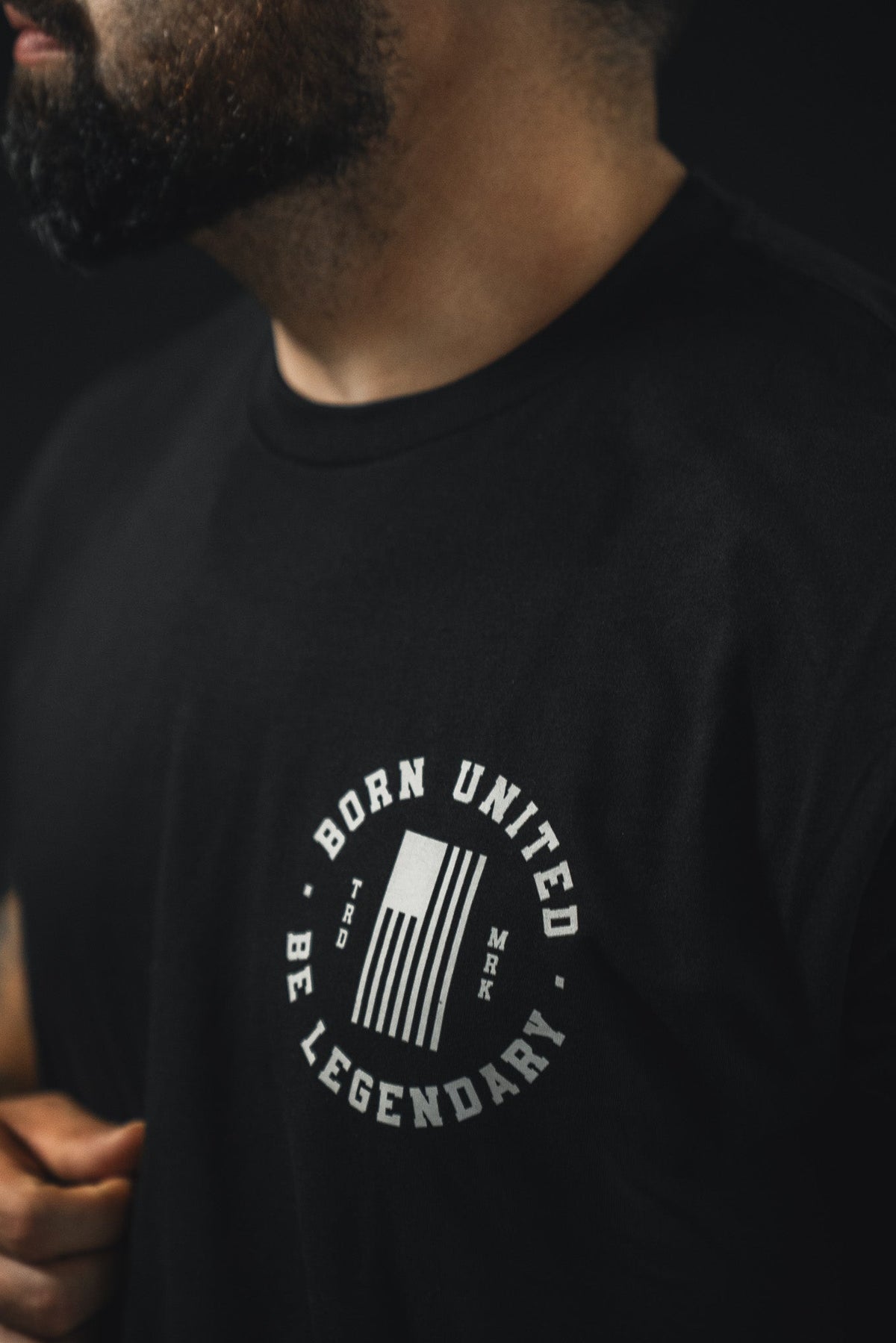 Wearing the Legend - Lincoln tee by Born United Private Label, featuring a white circular "BORN UNITED BE LEGENDARY" logo with a stylized flag and MRK TBD letters. The person's face is partially out of frame.