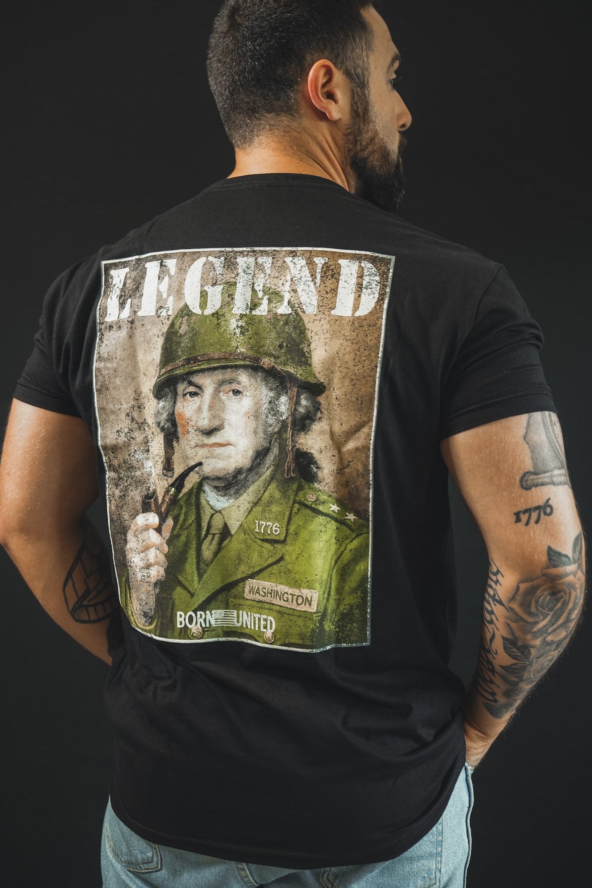 A man, his back to the camera, wears the Born United Private Label "Legend - Washington" tee—a black shirt with a military uniform illustration and "LEGEND" above. Tattoos cover both his arms, making it ideal for history fans.