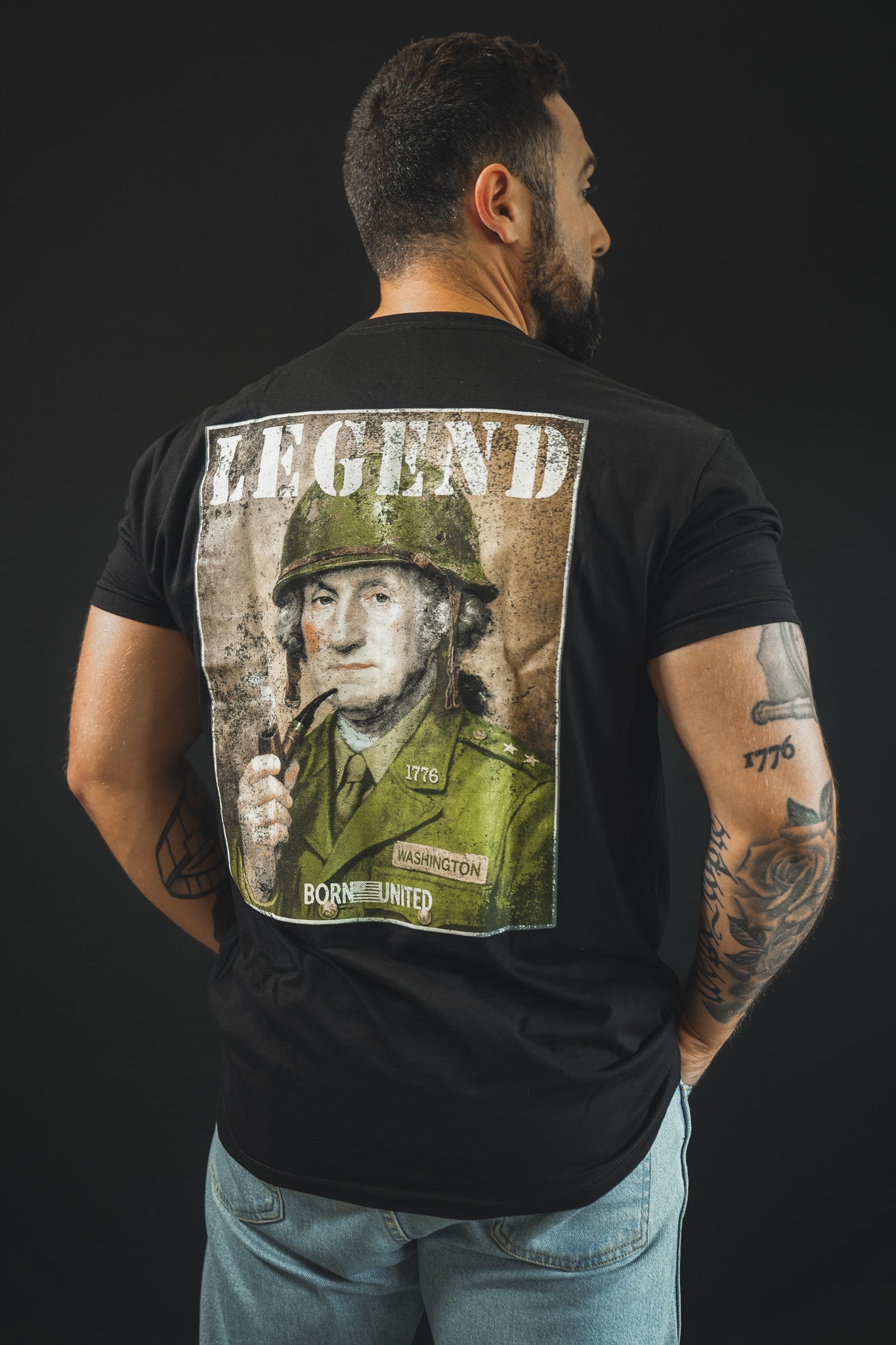 A man, his back to the camera, wears the Born United Private Label "Legend - Washington" tee—a black shirt with a military uniform illustration and "LEGEND" above. Tattoos cover both his arms, making it ideal for history fans.