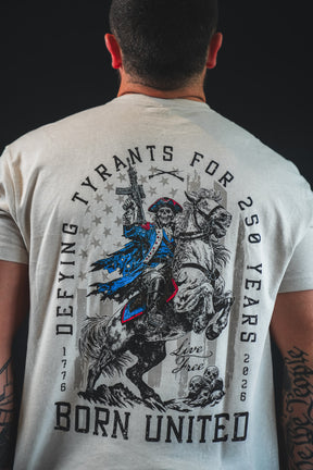 A man wears the Born United Private Label 250th Anniversary Tee, featuring a revolutionary soldier on horseback with "Defying tyrants for 250 years, 1776-2026, live free, born united." Celebrate American resilience in this special edition.