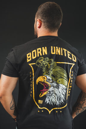 A tattooed man stands facing away, wearing The Eagle’s Scream tee by Born United Private Label—a black shirt with a bold bald eagle in a military helmet and "BORN UNITED" in yellow above, showing his American pride.