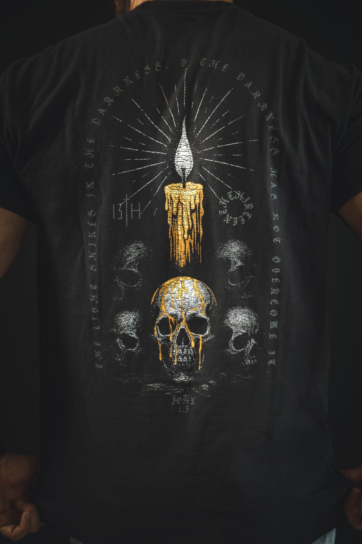 A person wears the 13th Victorious Dawn Premium Tee, featuring a golden melting candle above a skull, smaller skulls, and cryptic circular text on the back—a bold symbol of spiritual strength.