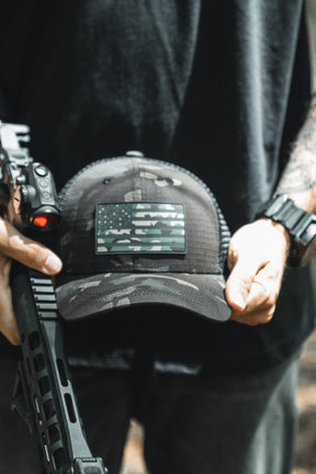Person holding a rifle and a tactical cap with a screen in a natural setting