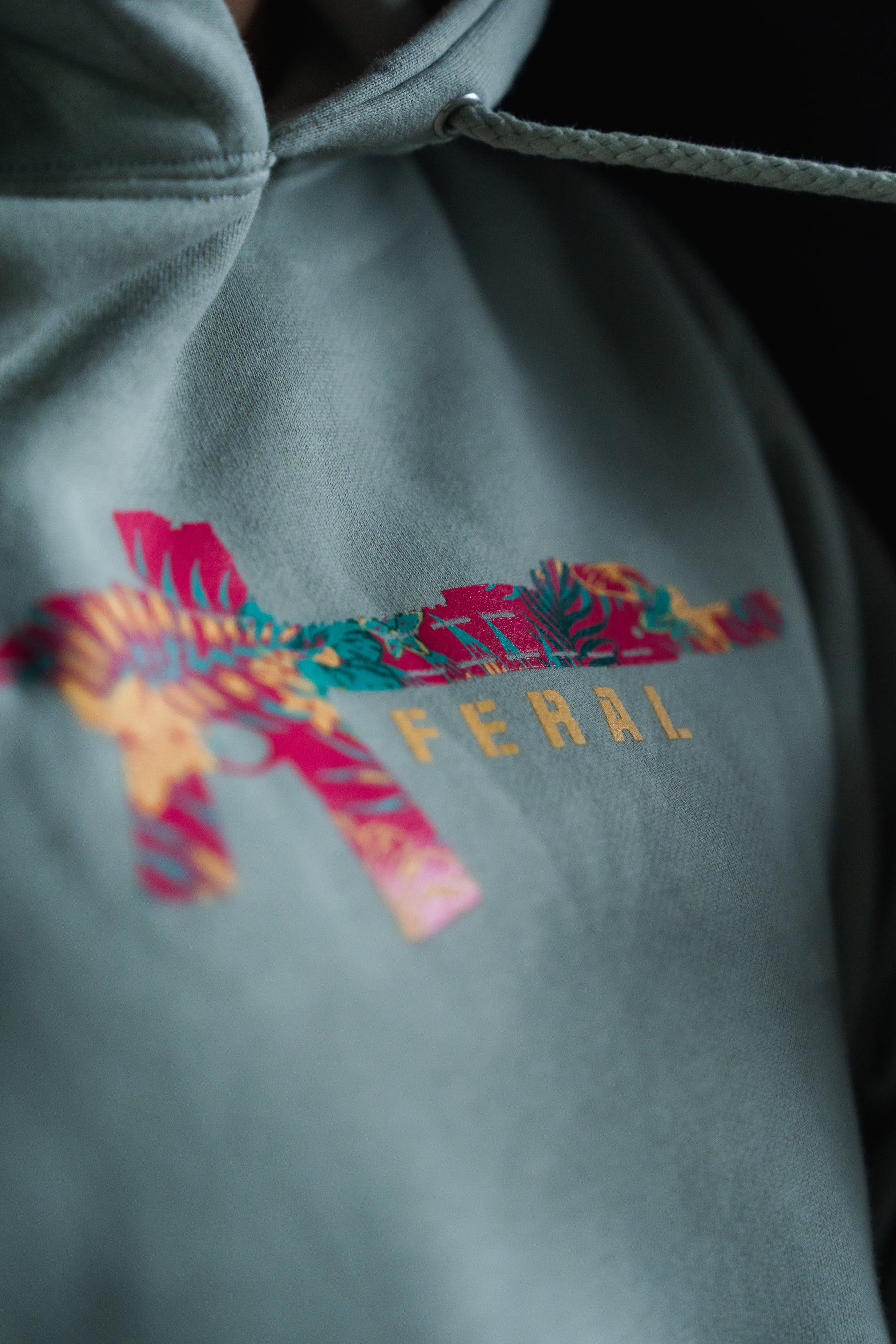 Feral - Premium Dusty Sage Hoodie featuring a rifle-shaped graphic filled with a floral print and the word FERAL printed underneath.