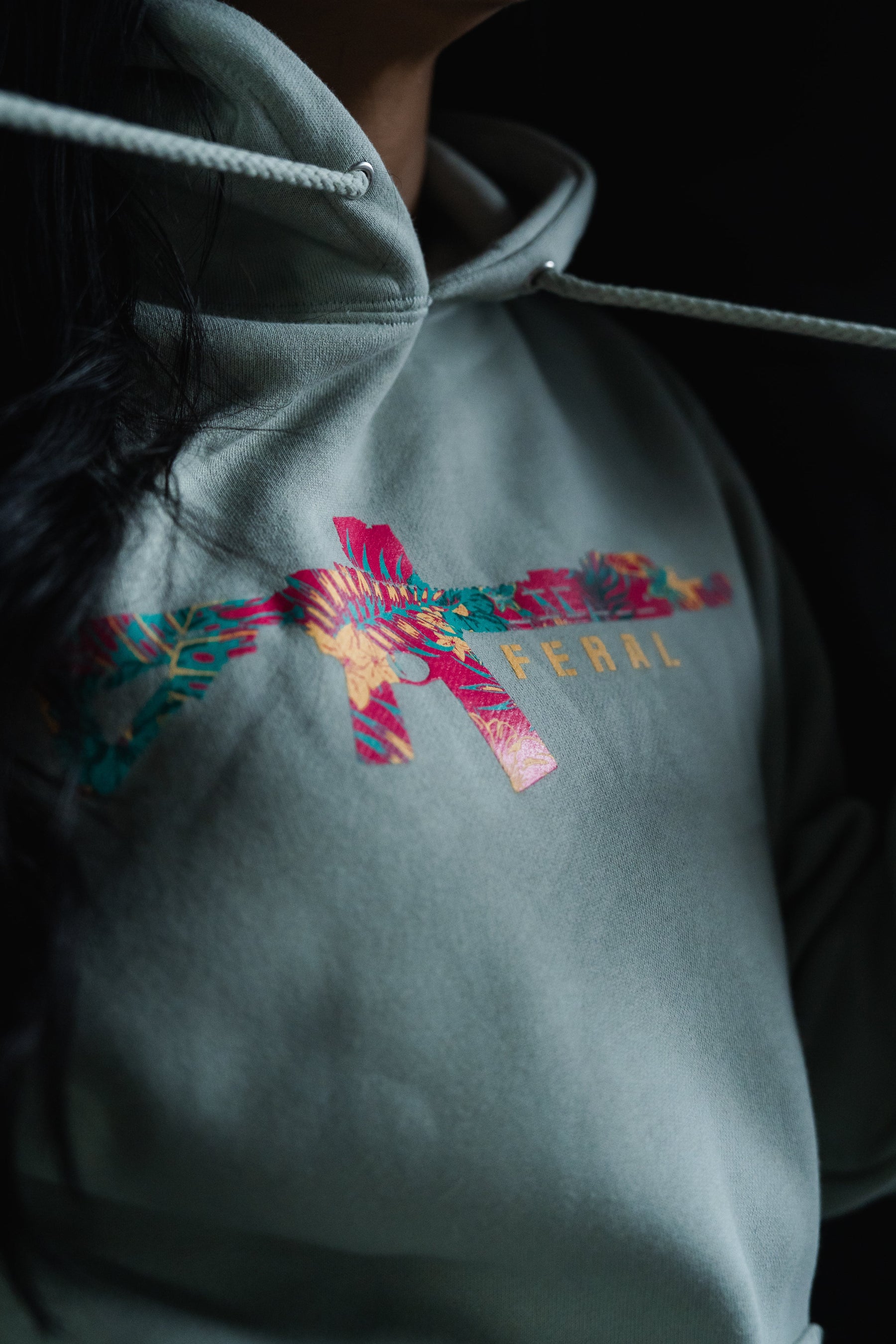 Feral - Premium Dusty Sage Hoodie in sage green, featuring a tropical floral rifle graphic and FERAL printed on the chest.