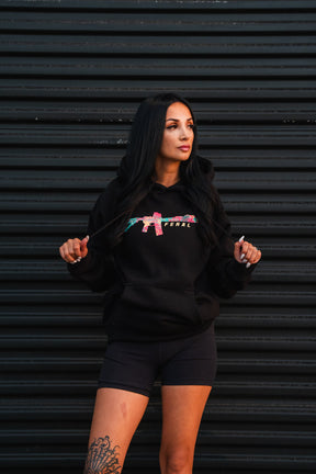 Woman wearing a black Feral - Premium Hoodie featuring a floral assault rifle graphic and FERAL branding, embodying a sense of radical authenticity.