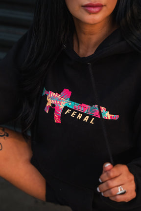 Feral - Premium Hoodie in black featuring a colorful, floral-patterned silhouette of a rifle with the word FERAL printed beneath it.