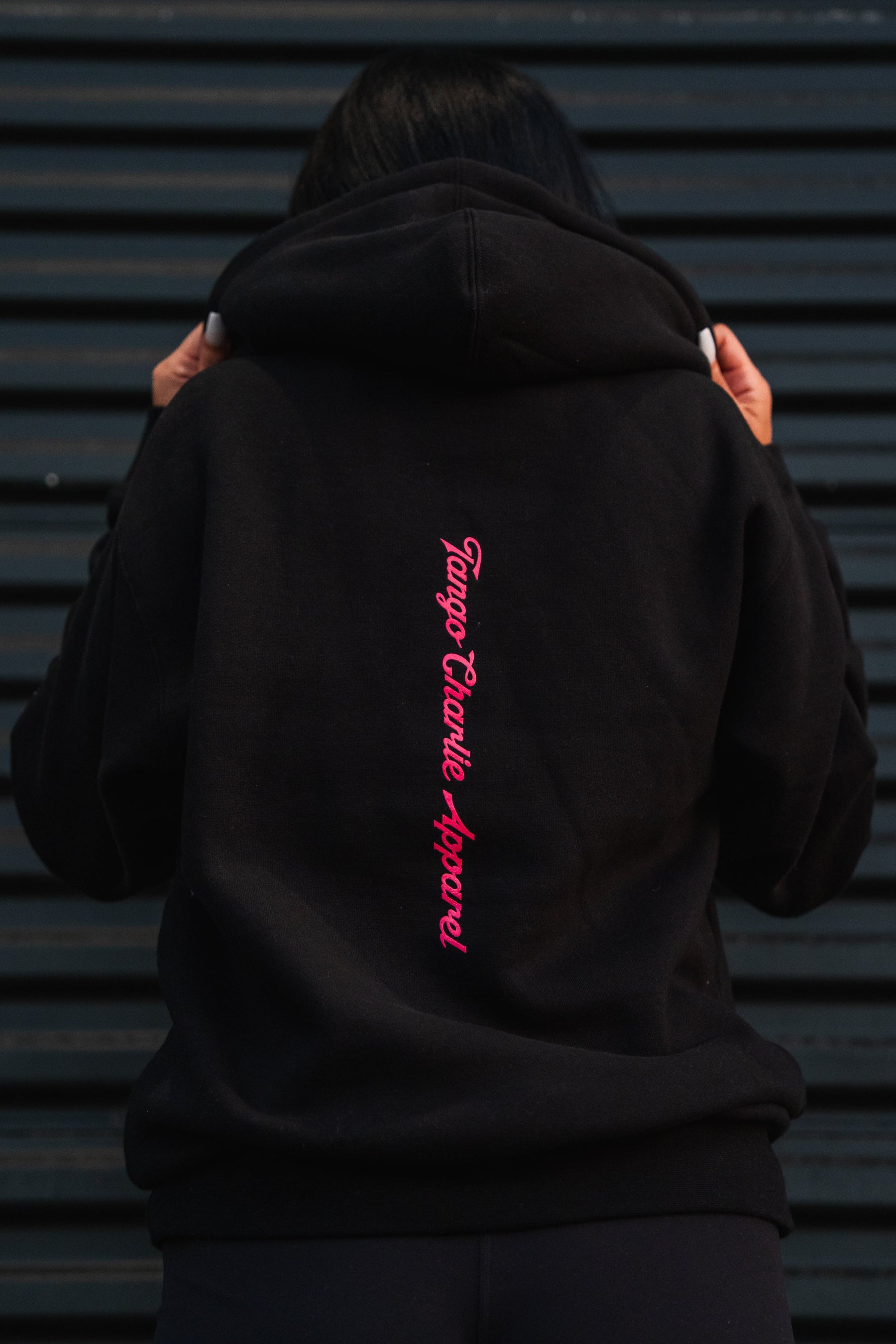 A person wearing a black Feral - Premium Hoodie with pink vertical text on the back, embodying a sense of feral wild and radical authenticity.