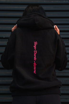 A person wearing a black Feral - Premium Hoodie with pink vertical text on the back, embodying a sense of feral wild and radical authenticity.