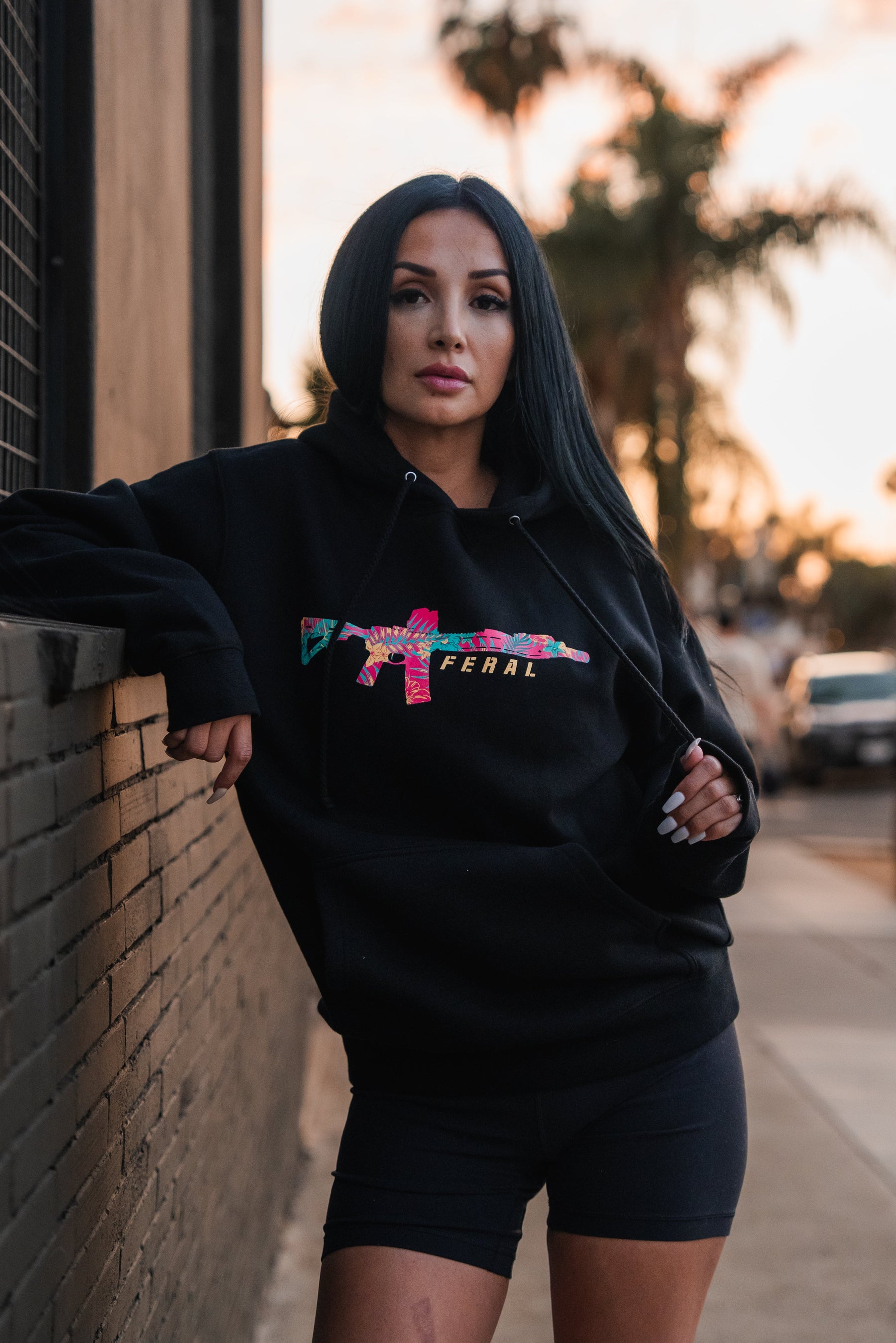 Woman wearing a black Feral - Premium Hoodie with a colorful, patterned rifle graphic and the word FERAL on the chest, capturing a sense of radical authenticity.