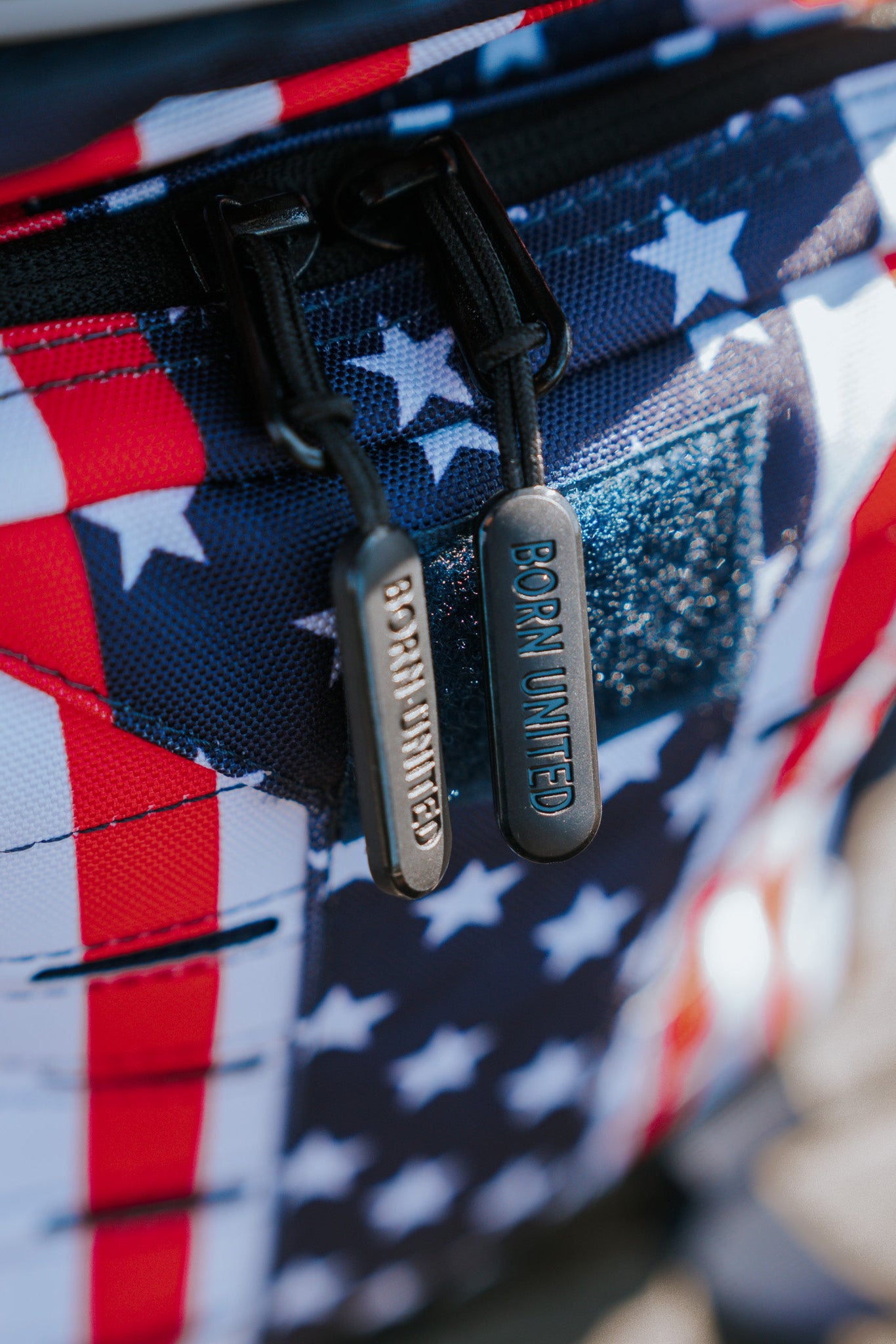 Close-up of the Ultimate Patriot Special Edition Tac-Pac - 25L by Born United Private Label, featuring a U.S. flag design with stars on a blue background and red and white stripes. Two zippers display BORN UNITED.