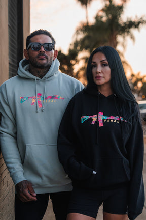 A man and woman wearing dusty sage Feral - Premium Dusty Sage Hoodies with a floral rifle graphic and the word FERAL across the chest.