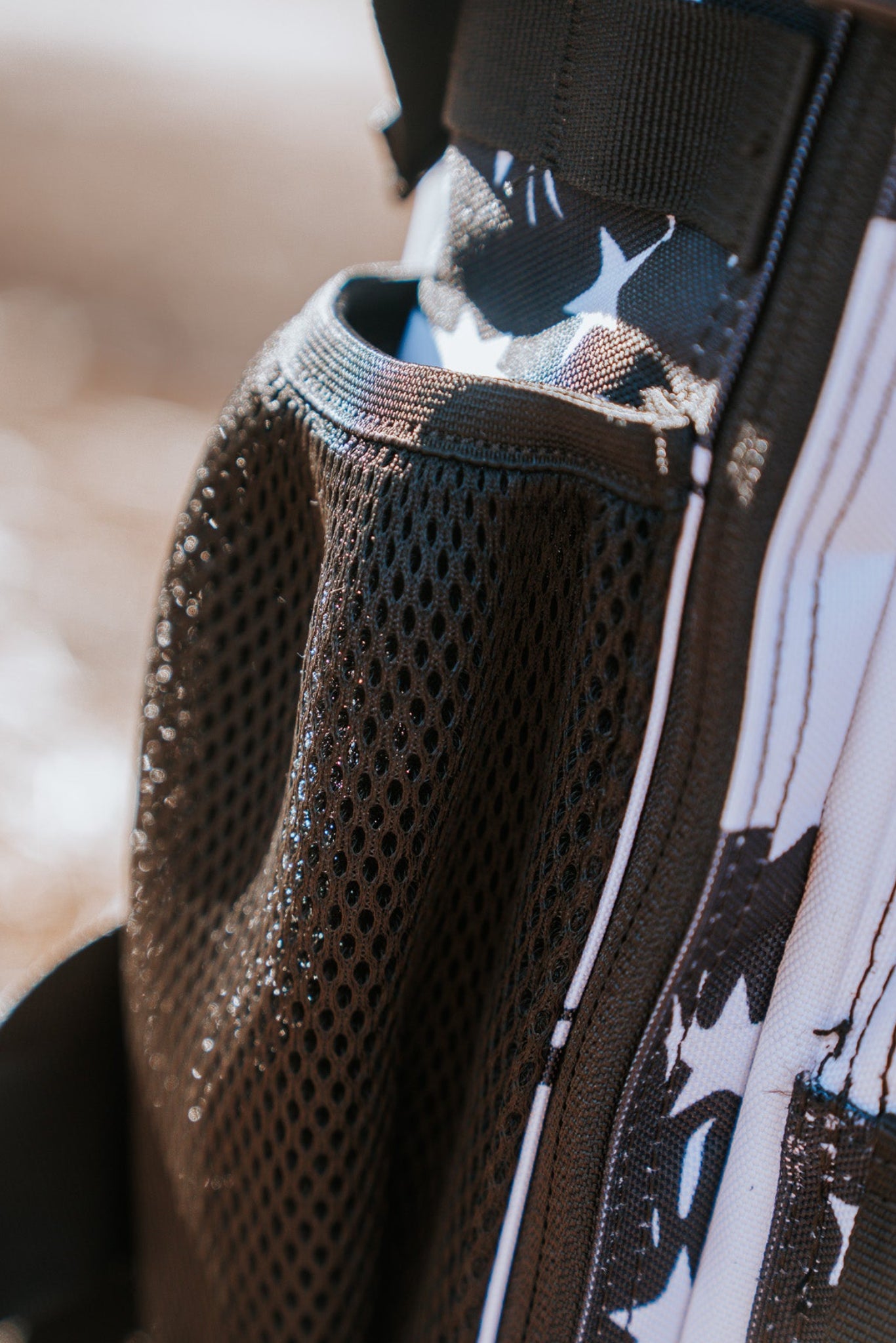 A close-up of the black mesh side pocket on the American Stealth Special Edition Tac-Pac - 25L by Born United Private Label emanates stealth vibes. Sunlight accentuates its texture, channeling the essence of stealth attire. The blurred background emphasizes this fashion-forward backpacks intricate details.