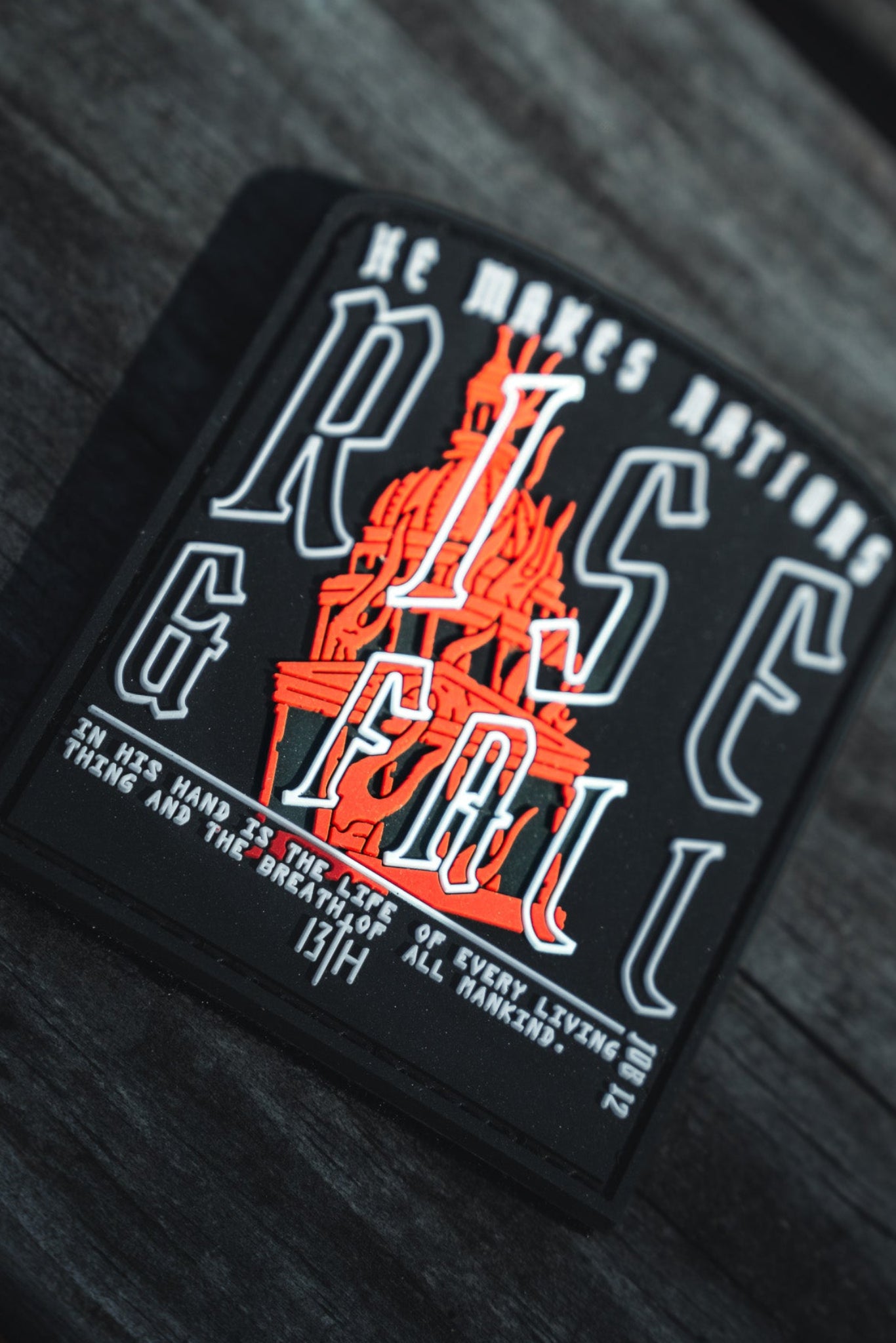 A black PVC patch from 13th, titled Rise And Fall, features an orange and black statue illustration with the phrase He makes nations rise and fall, alluding to thirteenth-century divine themes.