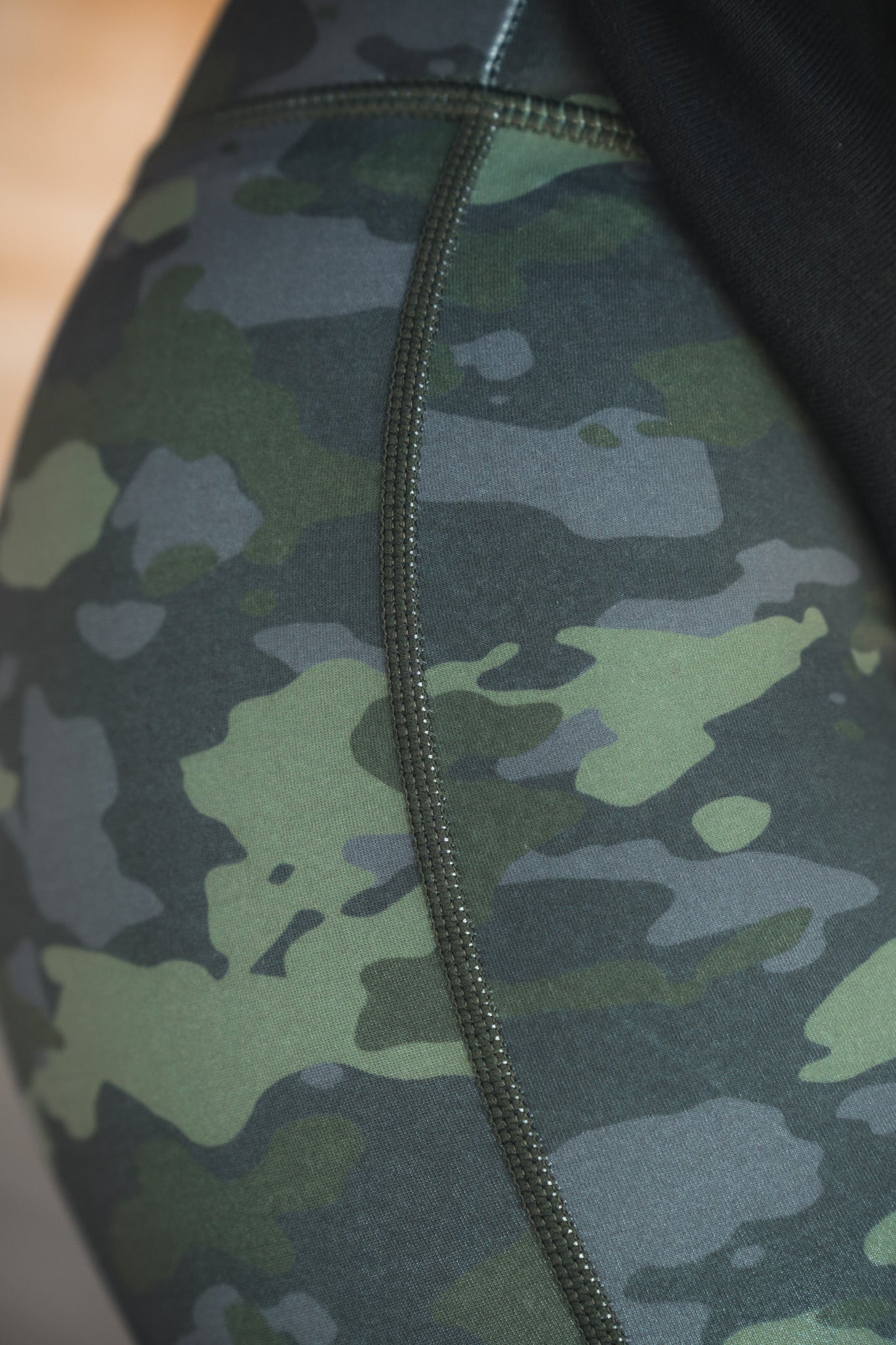 A close-up of someone wearing Combat Camo Leggings by Born United Private Label shows visible side seam stitching against a softly blurred backdrop.