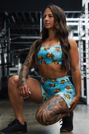 Woman in a blue patterned sports outfit posing in a gym.