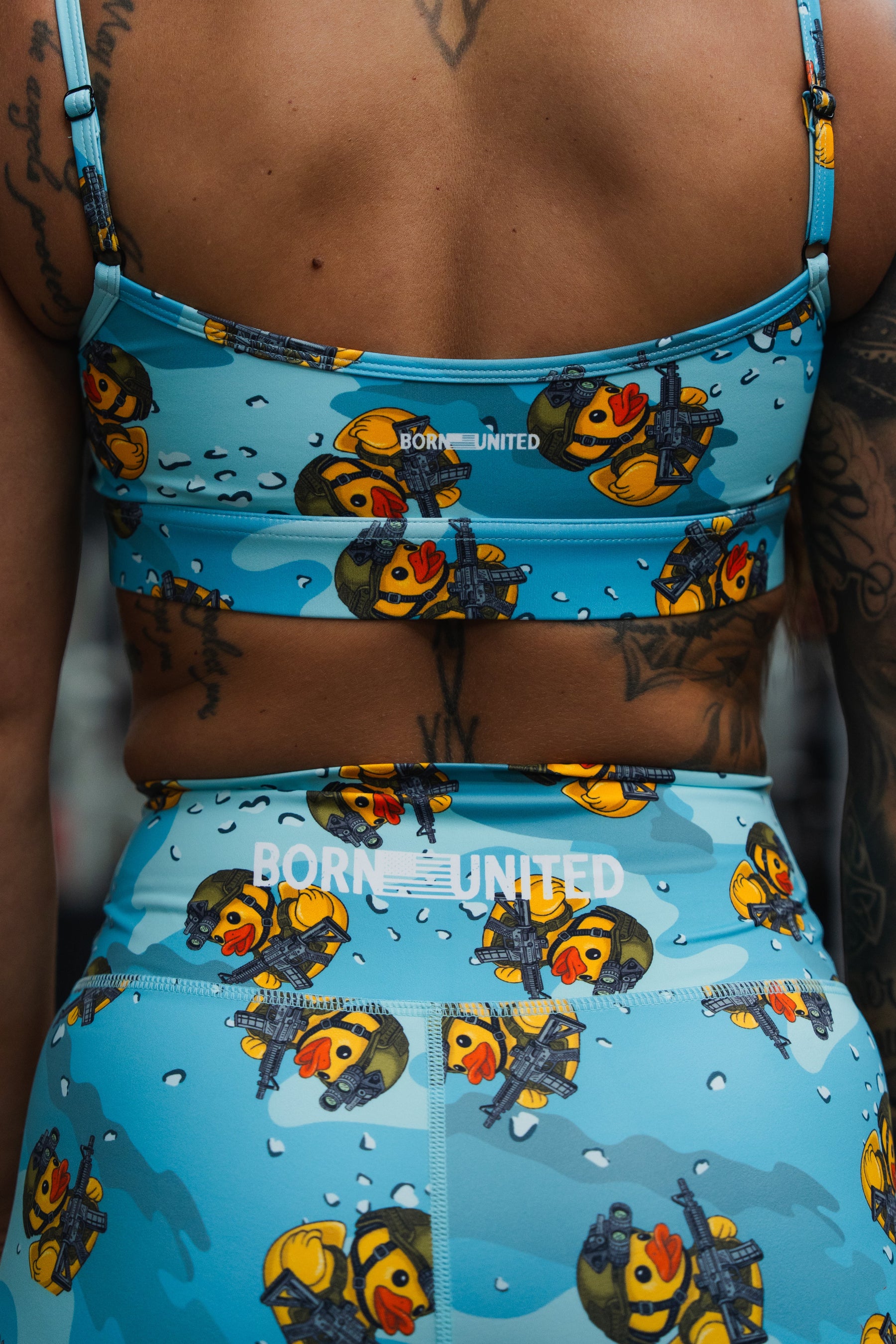 A person sports BORN UNITED's Women's High-Waisted Seamless Front Compression Training Shorts | Tacti-Quack, featuring cartoon duck and scuba diver prints. Visible tattoos on their back and arm highlight the bold design.