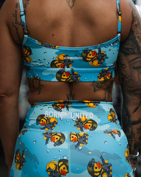 A person in a blue athletic outfit with cartoon duck and bubble designs sports the Born United Private Label Women's High-Waisted Seamless Front Compression Training Shorts (Tacti-Quack) and a matching sports bra, displaying tattoos on their arms and back.