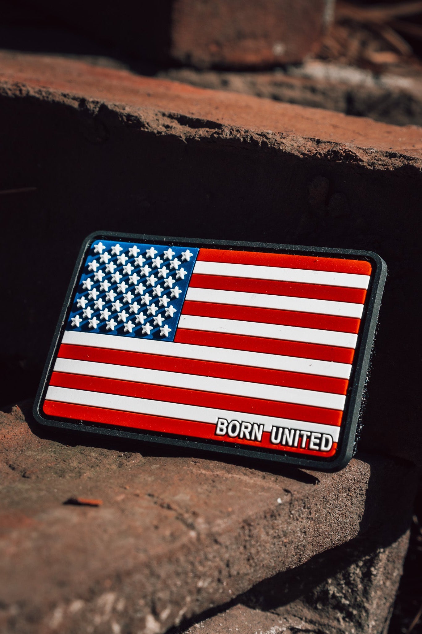 The American Flag PVC Patch from Born United Private Label, featuring a durable hook & loop design, proudly sits on rustic brick steps, showcasing its waterproof and washable features.