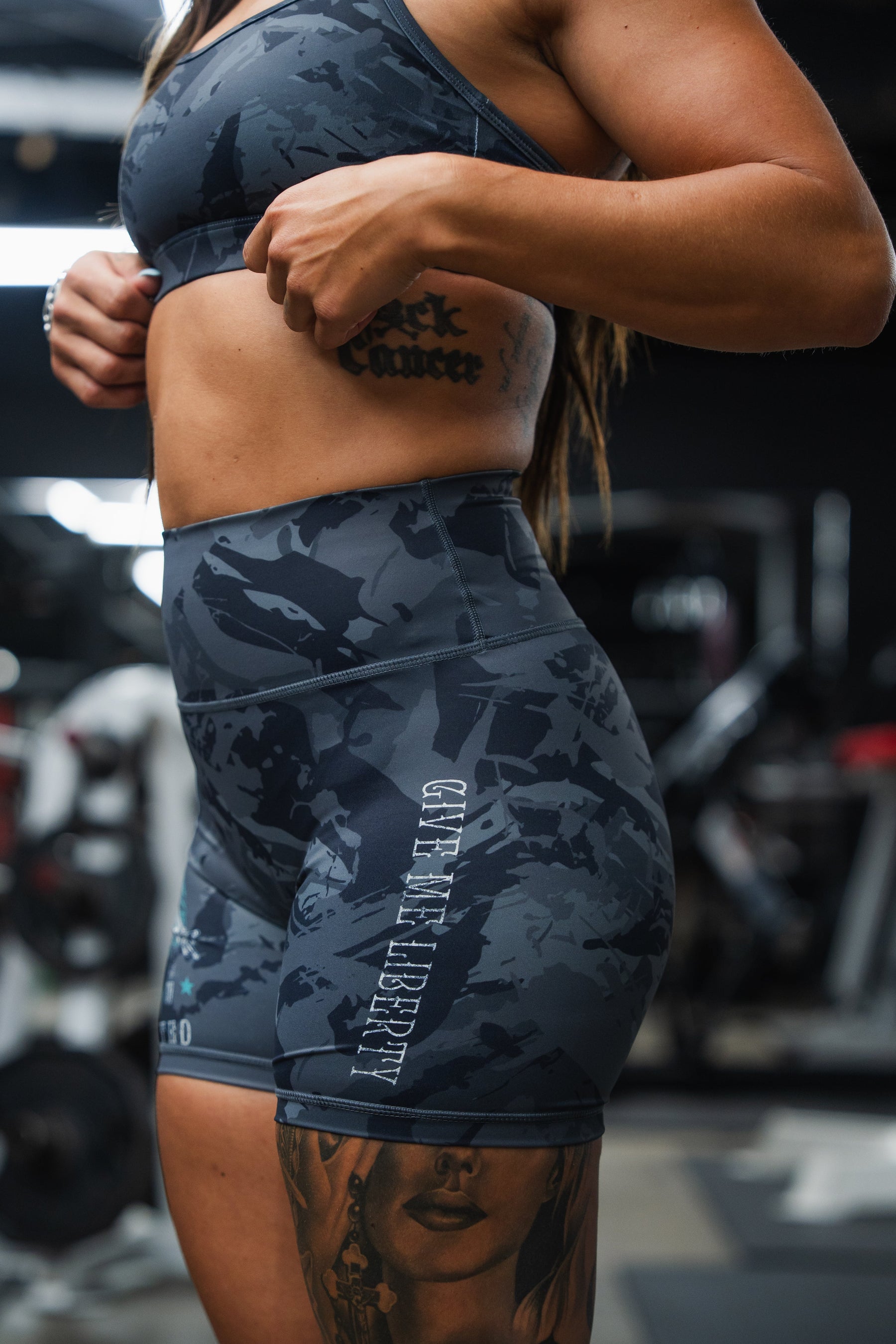 Person wearing dark gray camouflage athletic shorts with visible branding in a gym setting.