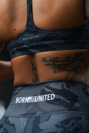 Close-up of a person's lower back in matching dark athletic wear with BORN UNITED and flag logo. A tattoo is visible above their Women's High-Waisted Seamless Front Compression Training Shorts | Liberty or Death by Born United Private Label.
