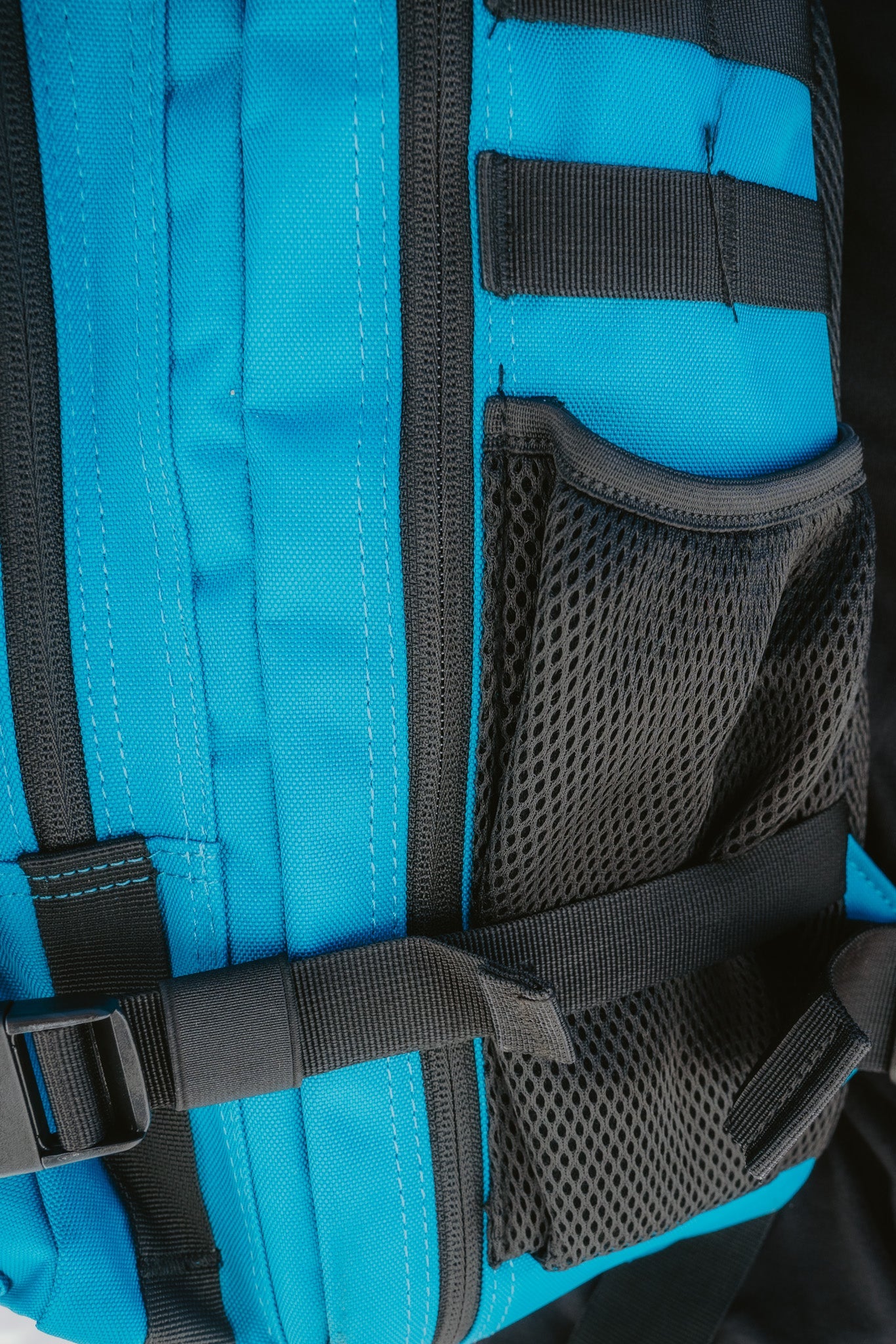 Close-up of the Electric Blue Premium Tac-Pac - 45L by Born United Private Label shows a durable electric blue and black backpack, featuring a mesh pocket, adjustable strap with buckle, and black stitching/details on vibrant blue sections.