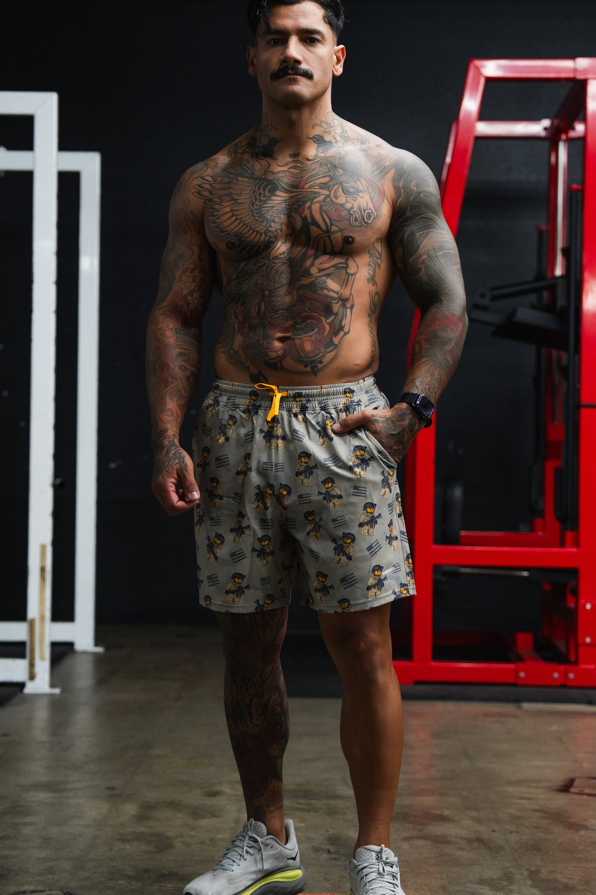 Muscular man in a gym wearing patterned shorts and sneakers.