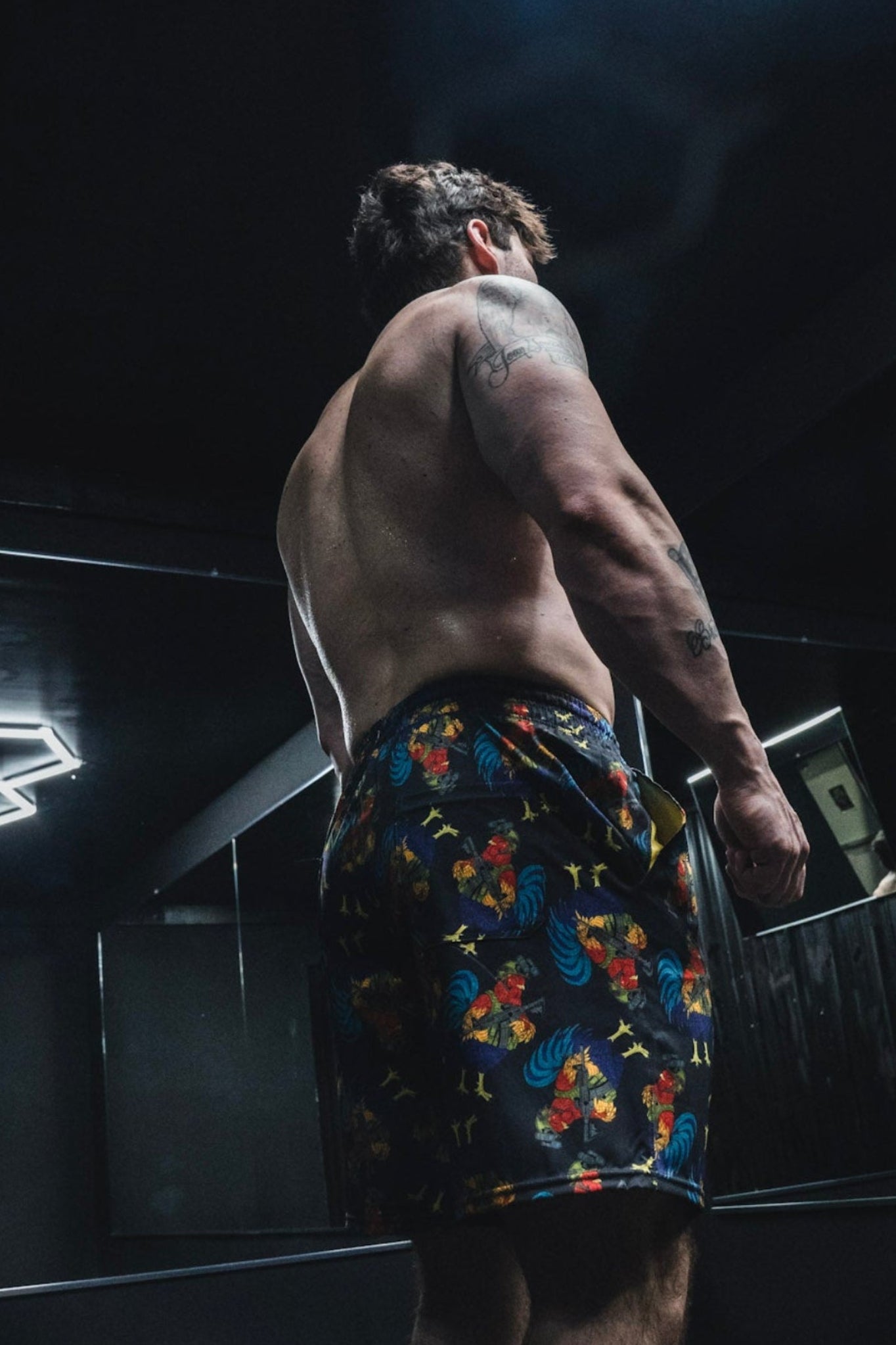 Man in colorful shorts standing in a dark room with neon lights.