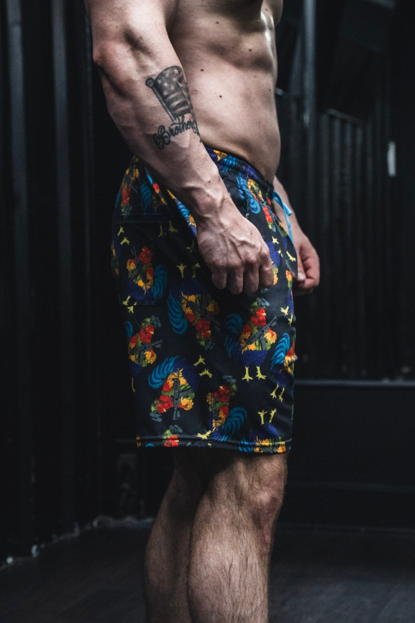 Person wearing colorful patterned shorts with tattoos on arms and chest.