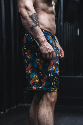 Person wearing colorful patterned shorts with tattoos on arms and chest.