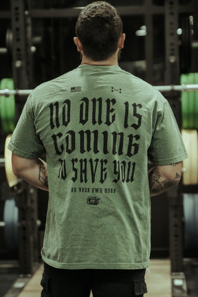Seen from behind in front of gym equipment, a person wears the Tango Charlie Apparel No One Is Coming To Save You Hemp - Premium Tee, featuring “NO ONE IS COMING TO SAVE YOU. BE YOUR OWN HERO” boldly printed on the back.