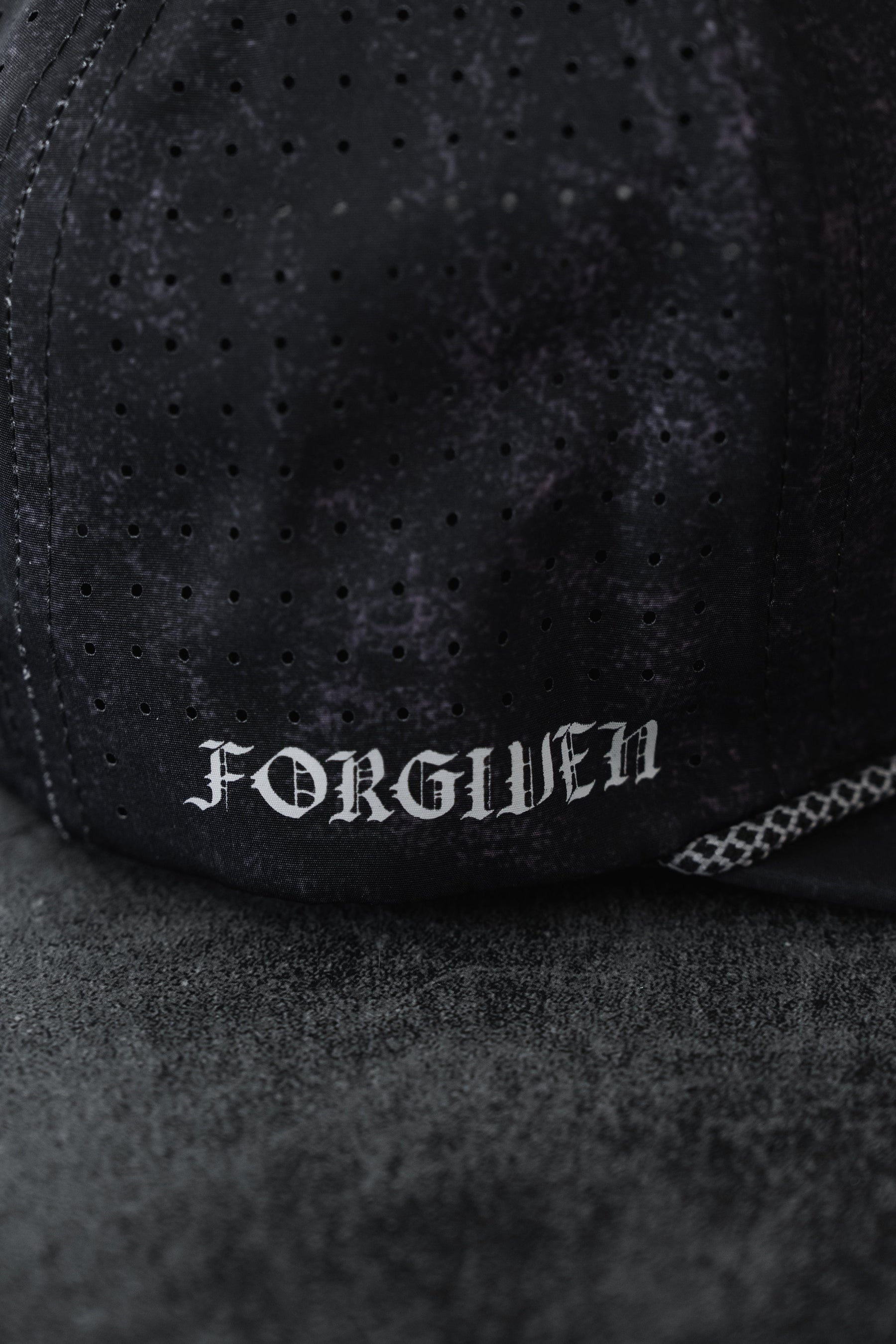 A close-up of the Relentless Betrayal Tattooed Child of God Mineral Wash PVC Snapback featuring black perforated fabric and "FORGIVEN" in white Gothic letters, from the premium Born United Private Label collection.