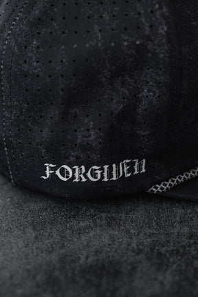 A close-up of the Relentless Betrayal Tattooed Child of God Mineral Wash PVC Snapback featuring black perforated fabric and "FORGIVEN" in white Gothic letters, from the premium Born United Private Label collection.