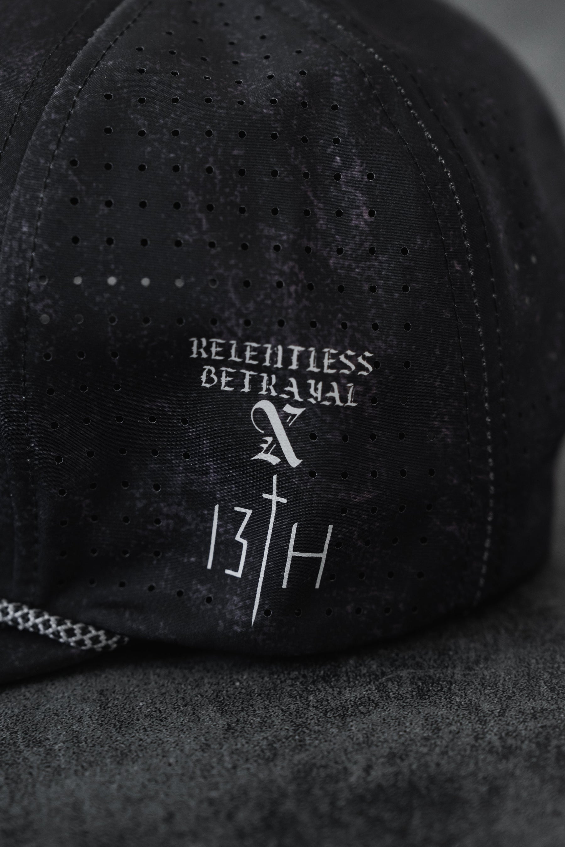 A close-up of a Tattooed Child of God Mineral Wash PVC Snapback by Relentless Betrayal, featuring white "RELENTLESS BETRAYAL" text above a stylized cross and "13TH" on the fabric.
