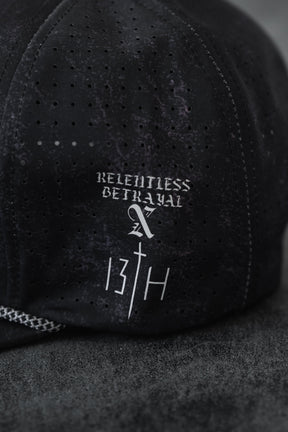 A close-up of a Tattooed Child of God Mineral Wash PVC Snapback by Relentless Betrayal, featuring white "RELENTLESS BETRAYAL" text above a stylized cross and "13TH" on the fabric.