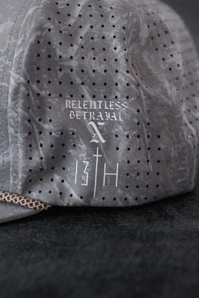 A close-up of the Relentless Betrayal Tattooed Child of God Deadwood Camo PVC Snapback, featuring white "RELENTLESS BETRAYAL" text and stylized 13TH graphics—ideal faith-inspired apparel for devoted fans.
