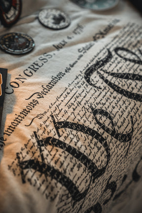 Close-up of fabric printed with the U.S. Declaration of Independence in decorative script, plus commemorative patches—perfect for America's 250th or adding to your Born United Patriot Box by Born United Private Label.