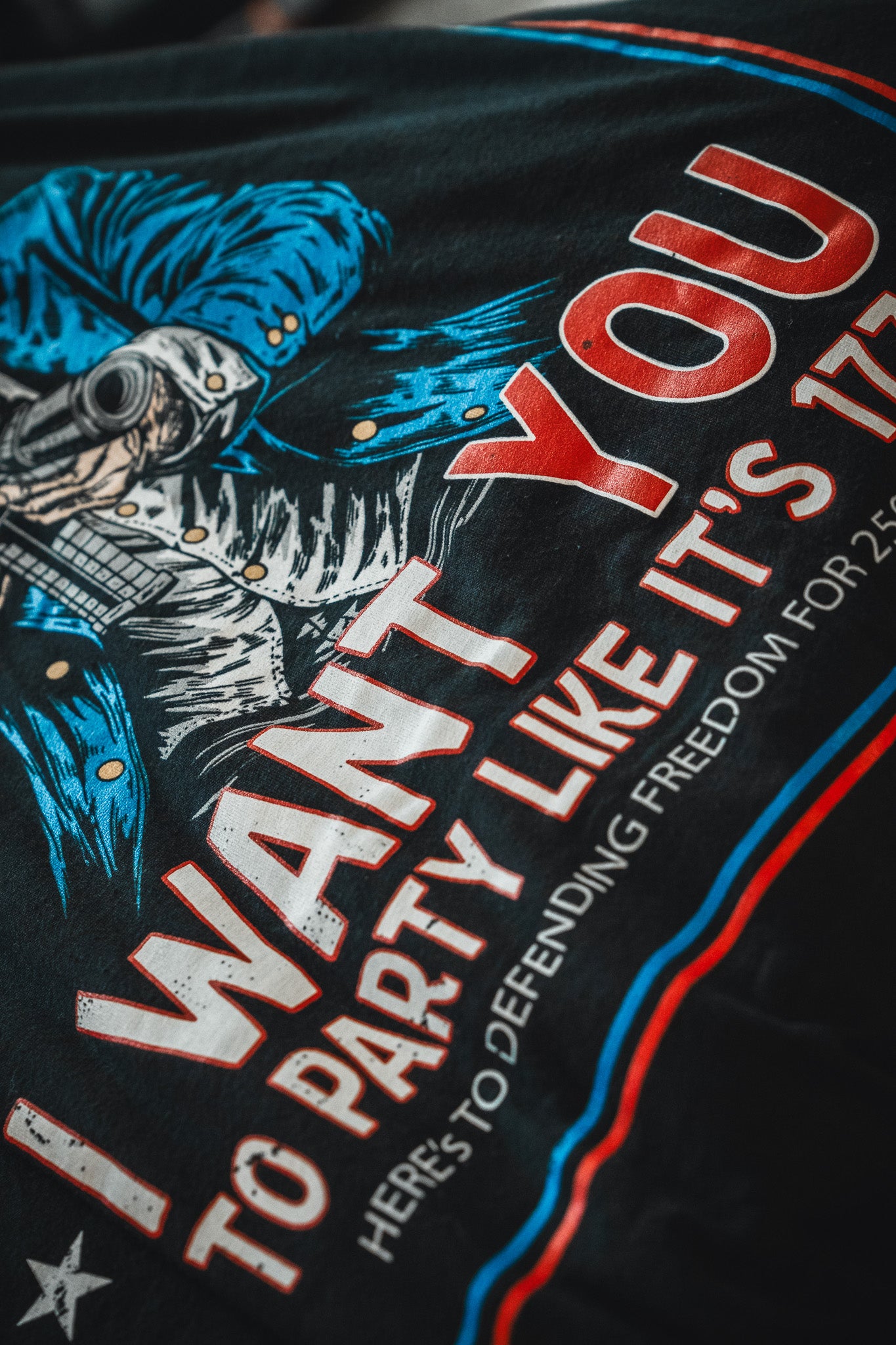 A close-up of the Born United Patriot Box T-shirt by Born United Private Label, featuring a person in military gear and “I WANT YOU TO PARTY LIKE IT’S 1776. HERE'S TO DEFENDING FREEDOM FOR 245 YEARS” in bold red, white, and blue—perfect for America's 250th Birthday.