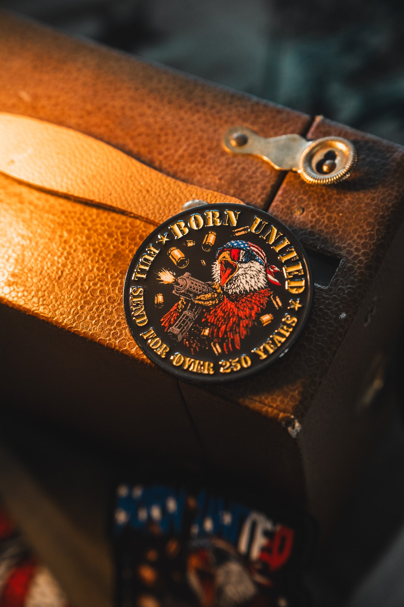 A round patch on brown leather shows an eagle in a bandana and jacket with the text "Born United" and "For Over 250 Years, Class Hero," celebrating America's 250th Birthday with the Born United Patriot Box by Born United Private Label.