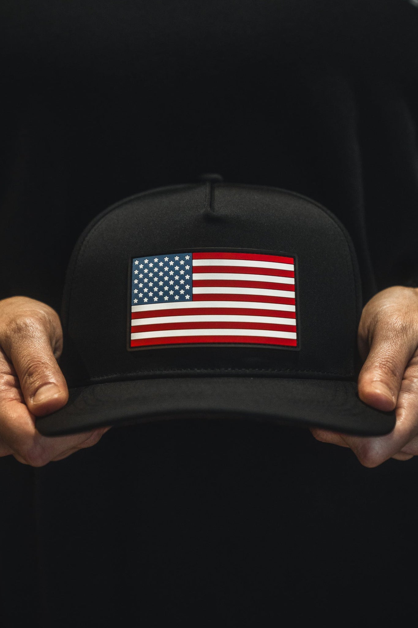Black cap with American flag held by a person wearing a black shirt.