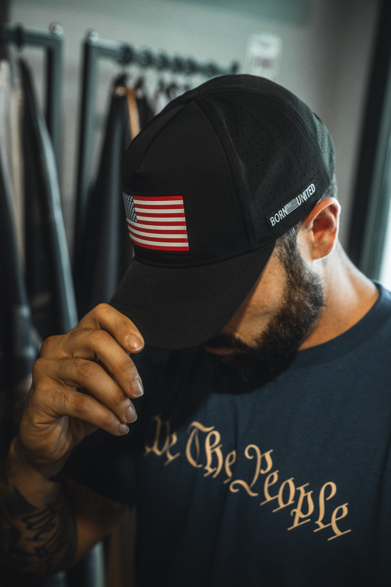 Man wearing a black cap with an American flag patch and a black t-shirt with 'We The People' text.