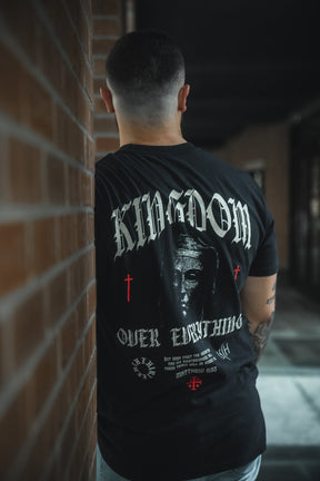 A man with short dark hair faces away, wearing the 13th's Kingdom Over Everything Premium Tee, featuring a bold “KINGDOM OVER EVERYTHING” graphic, a face design, and red crosses on the back.