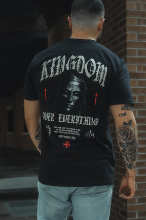 Person wearing a black t-shirt with 'Kingdom Over Everything' text and graphics, standing in front of a brick wall.