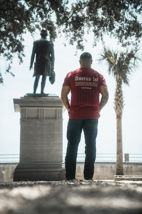 Person wearing a red t-shirt with text standing in front of a statue
