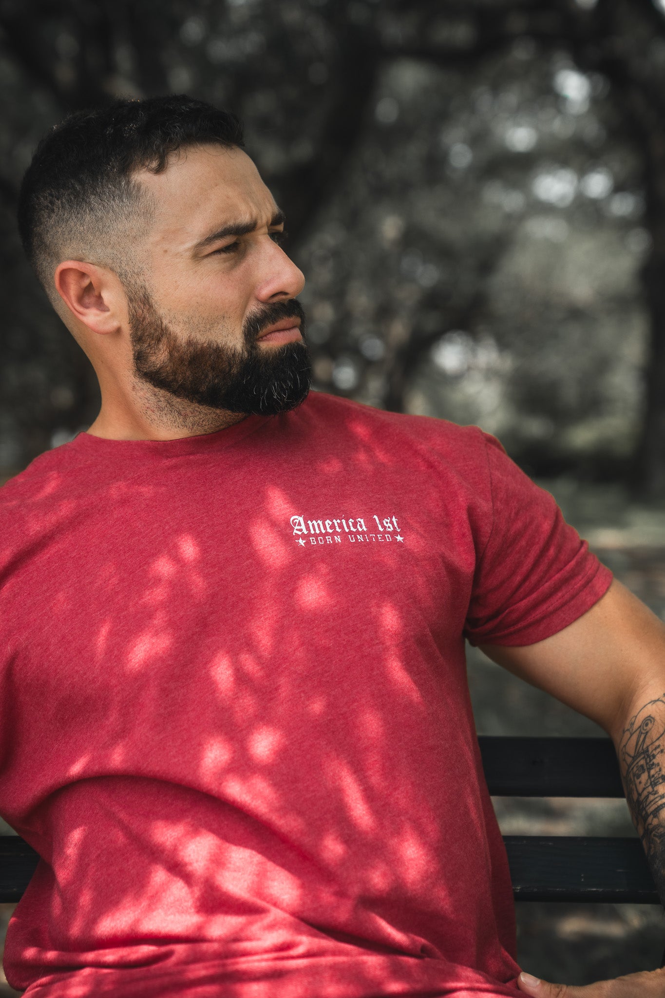 Man wearing a red t-shirt with text, sitting outdoors with trees in the background